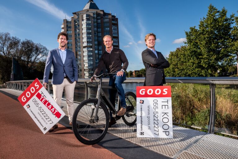 Makelaars van GOOS Makelaardij op een brug in Apeldoorn met TE KOOP-bord